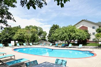A pool surrounded by trees and chairs.